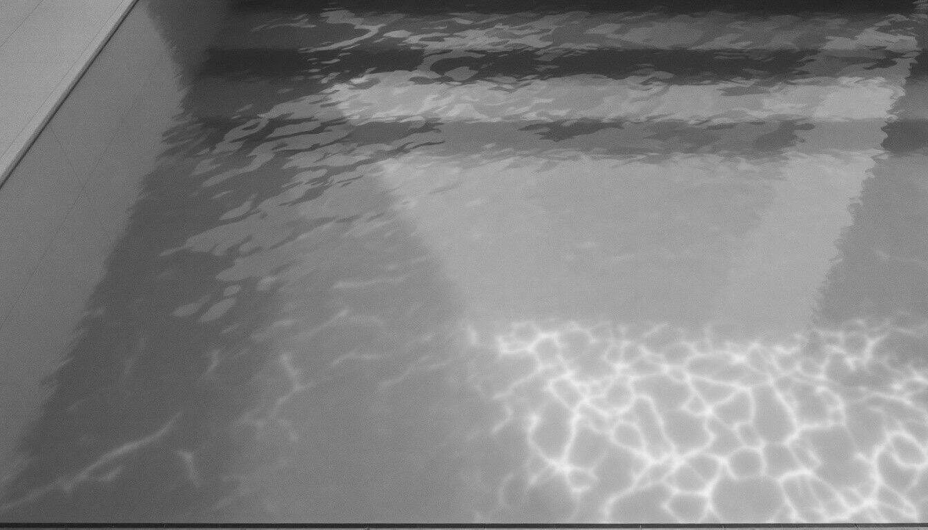 Vue de dessus d’un bassin d’eau limpide aux marches blanches, dans un mikvé moderne sobre et lumineux